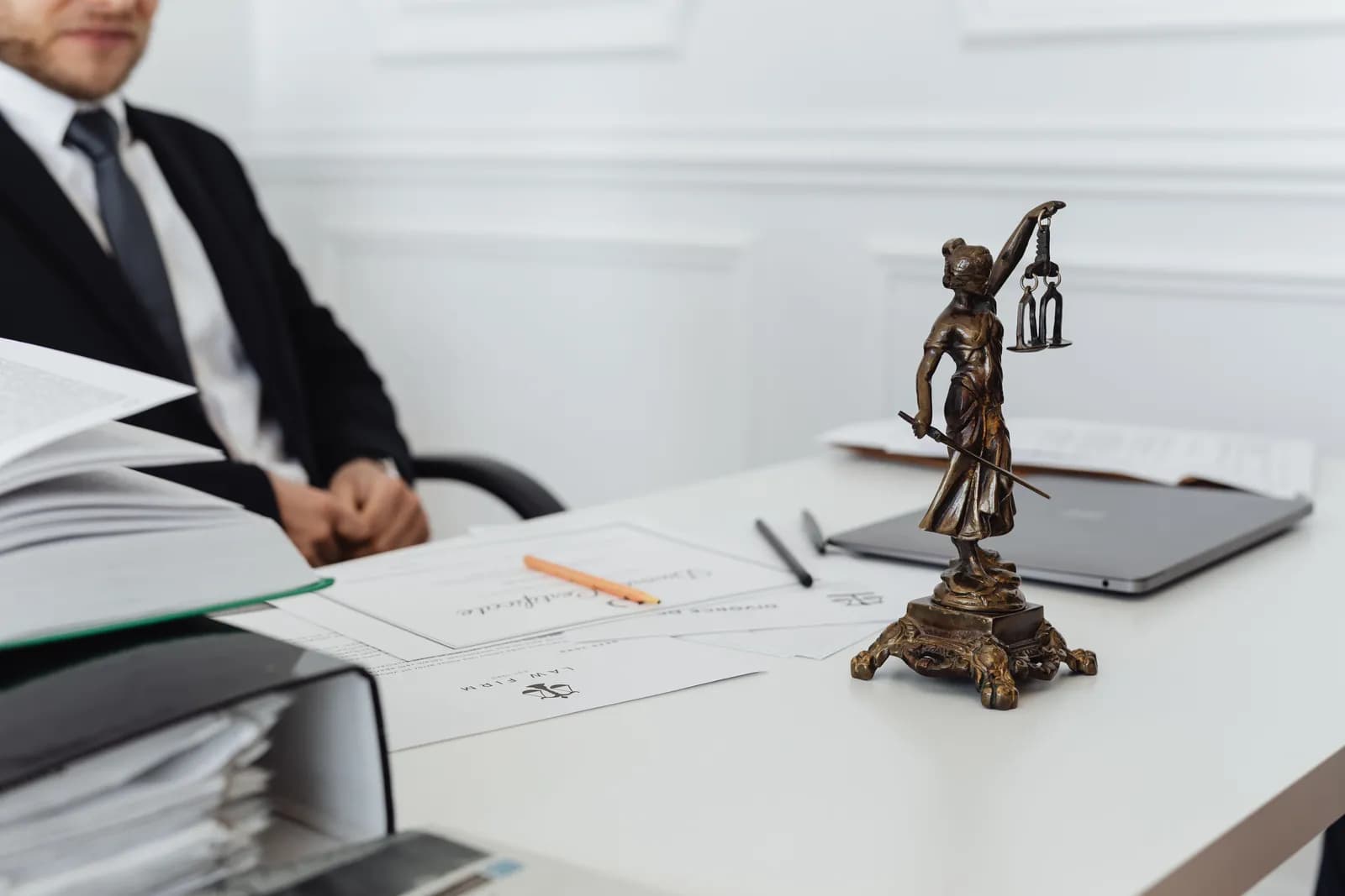Commissaire de justice à son bureau, dossiers de recouvrement et statue de la justice